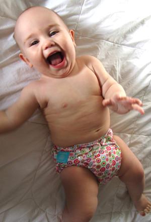 Smiling baby laying on bed in Charlie Banana Reusable Cloth Diaper